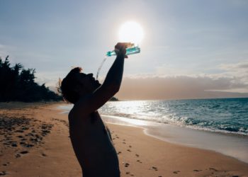 Un hombre bebe agua en una playa. Foto Pxhere.