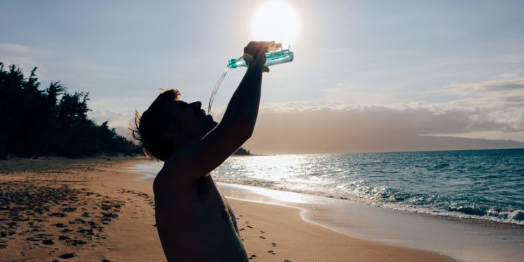 Un hombre bebe agua en una playa. Foto Pxhere.