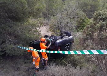 El coche volcado en una curva en la carretera Jesús-Cala Llonga. Los operarios de Grúas Ibiza lo inspeccionan para retirarlo