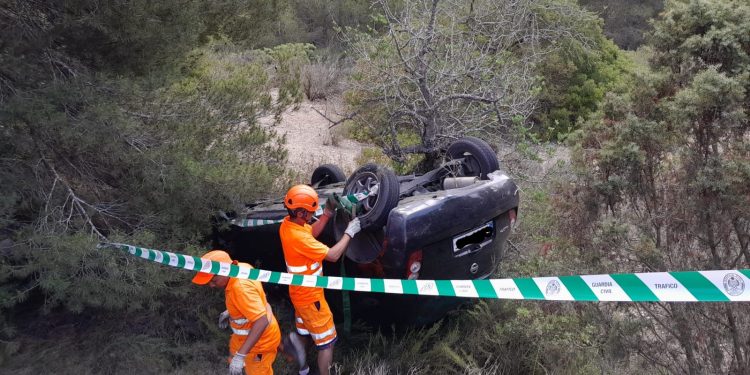 El coche volcado en una curva en la carretera Jesús-Cala Llonga. Los operarios de Grúas Ibiza lo inspeccionan para retirarlo