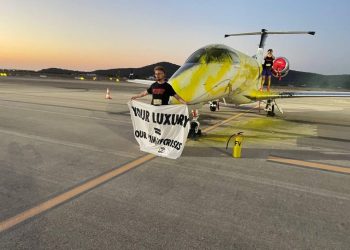Uno de los activistas despliega una pancarta junto al jet que rociaron de pintura en el aeropuerto de Ibiza en julio de 2023.