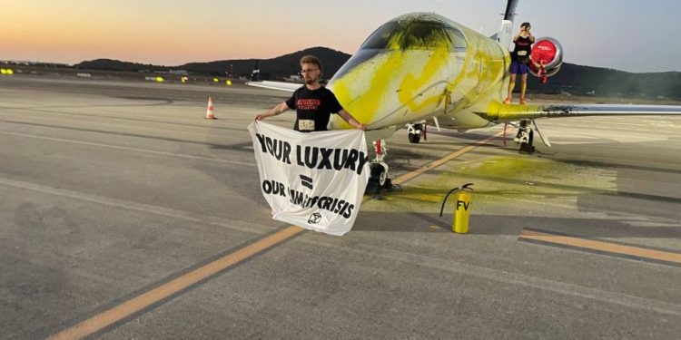 Uno de los activistas despliega una pancarta junto al jet que rociaron de pintura en el aeropuerto de Ibiza en julio de 2023.