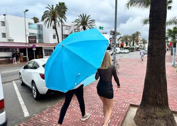 Turistas bajo la lluvia con una sombrilla de playa.