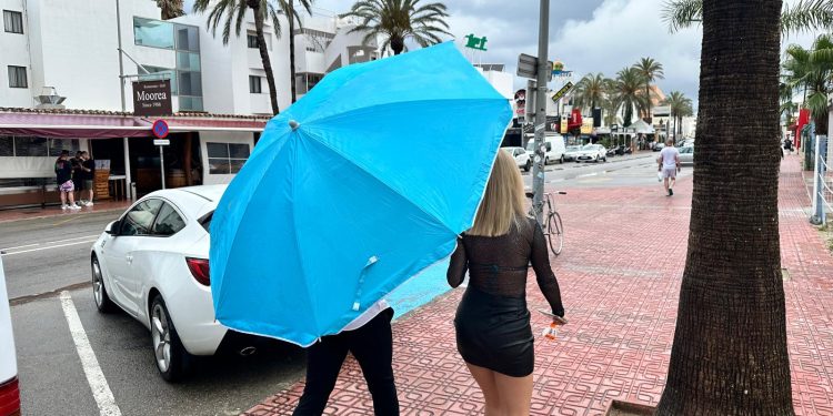 Turistas bajo la lluvia con una sombrilla de playa.