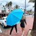 Turistas bajo la lluvia con una sombrilla de playa.