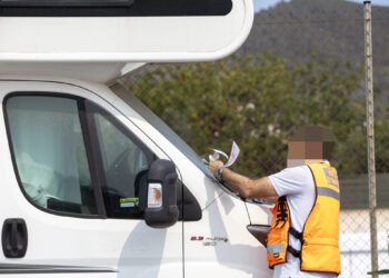 Un agente coloca un aviso de retirada y posible multa a una autocaravana estacionada.