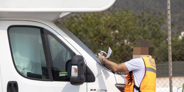 Un agente coloca un aviso de retirada y posible multa a una autocaravana estacionada.