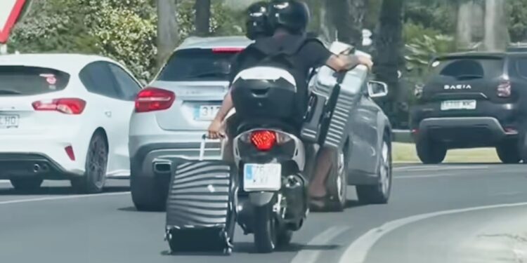 Dos motoristas llevan dos maletas sobre la moto, una de ellas arrastrando las ruedas  por la carretera, en este vídeo compartido en @ibizatheparadise cuenta de Instagram