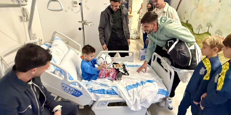 Los jugadores de la Penya ofrecen unos detalles a uno de los niños ingresados. / SCR Penya Deportiva