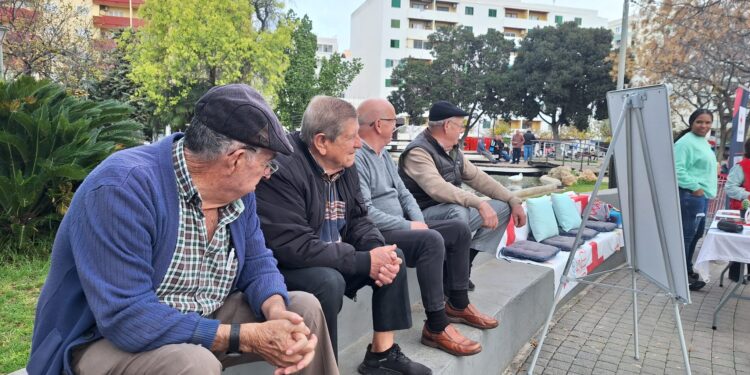 Cuatro jubilados escuchan la música que suena en el altavoz del puesto de la Cruz Roja. / D.V.