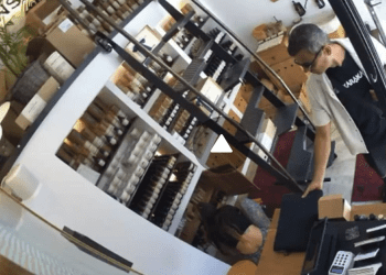 Captura de la cámara de seguridad del establecimiento que capta perfectamente al hombre llevándose del ordenador mientras la empleada, agachada, coloca mercancía en unos estantes. Imágenes cedidas a Noudiari